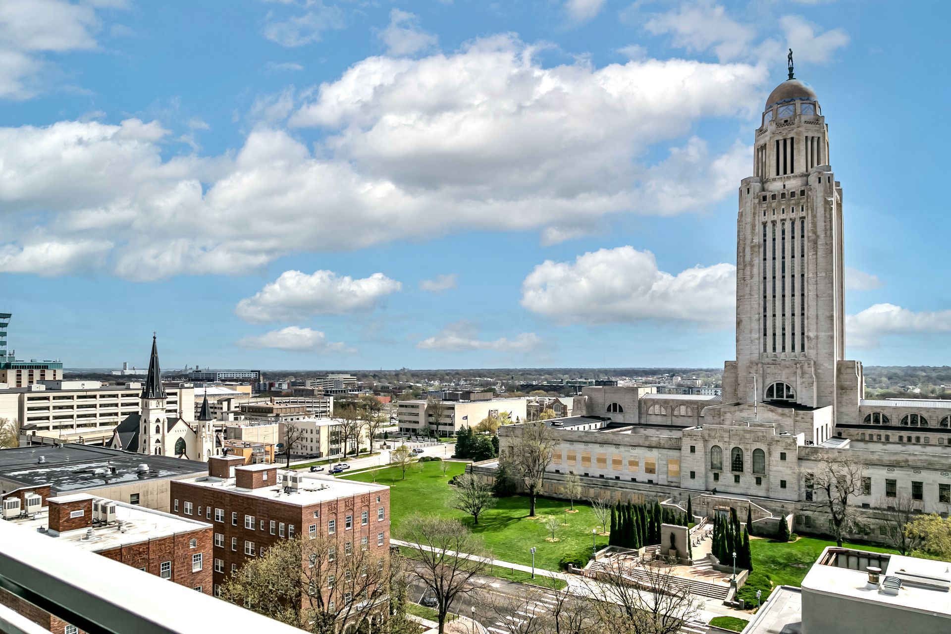View of downtown skyline with a tall historic tower beside a green park under a cloudy blue sky
