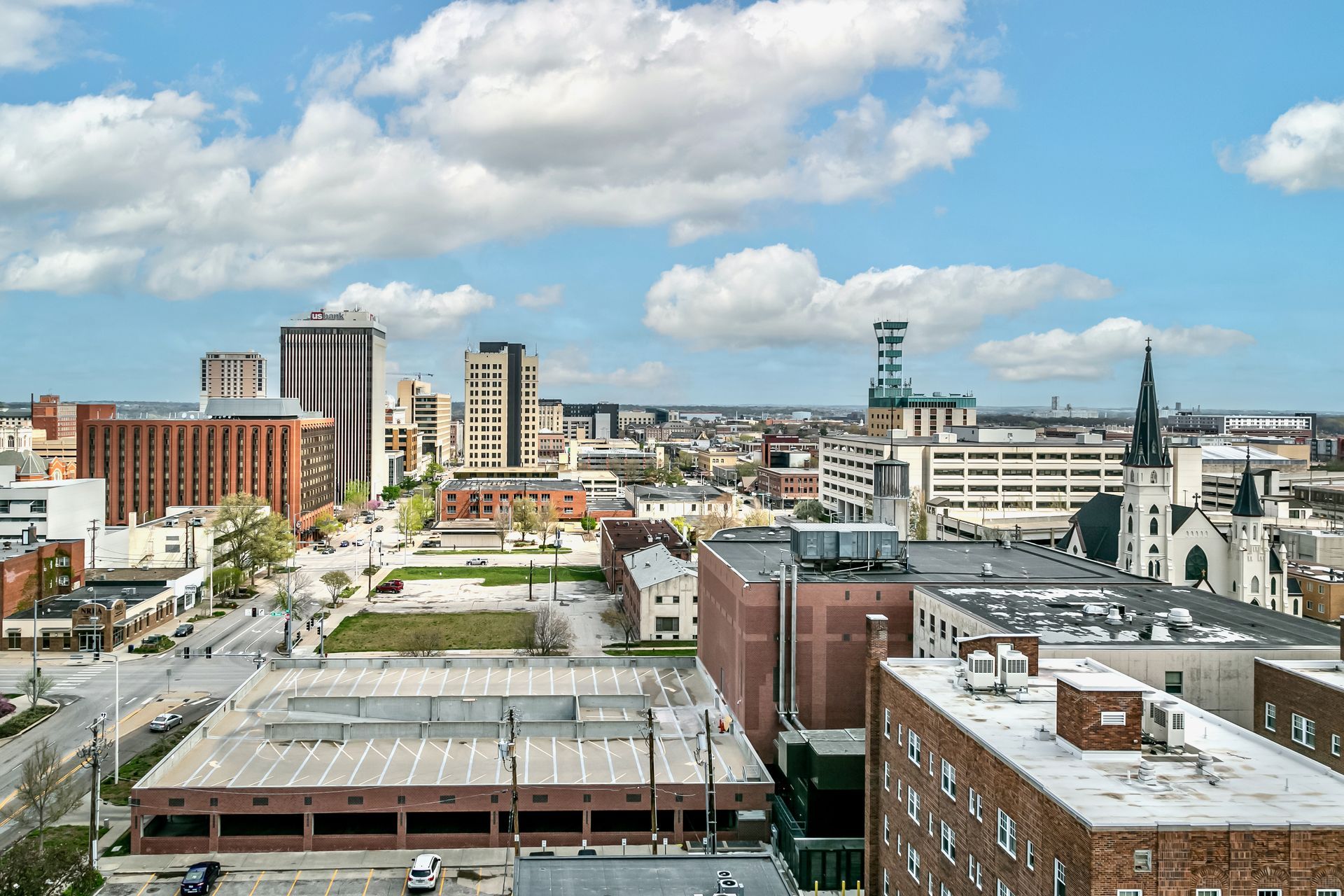 Downtown city skyline with mid-rise buildings, church spires, and a blue sky with clouds