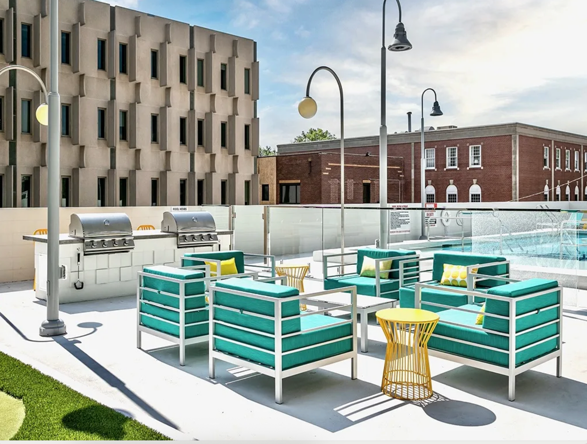 Rooftop pool deck with turquoise lounge seating, grills, and city buildings in the background