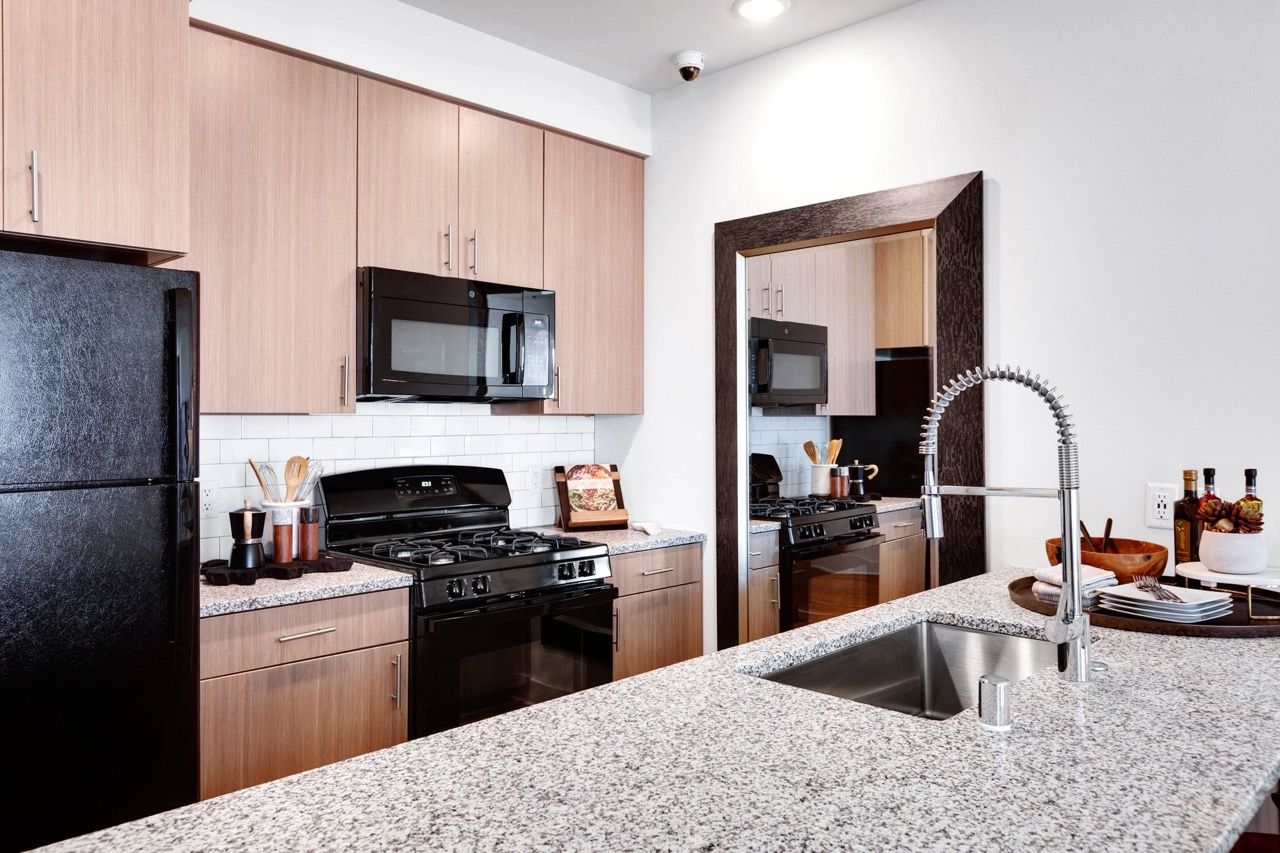 Modern kitchen in an apartment with wooden cabinets, granite countertops, stainless steel appliances, and a large sink.