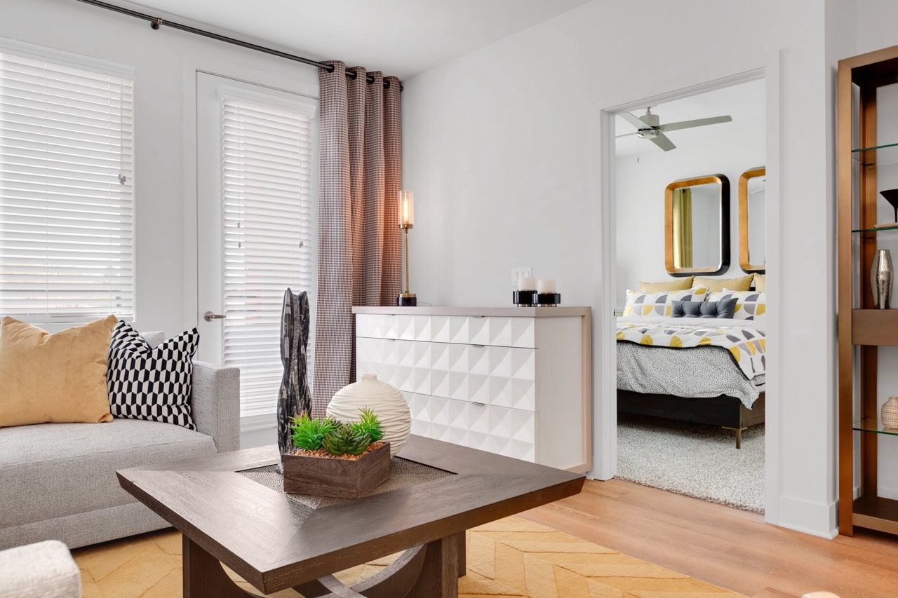 Bright living room in an apartment with a beige sofa, coffee table, and doorway to a bedroom.