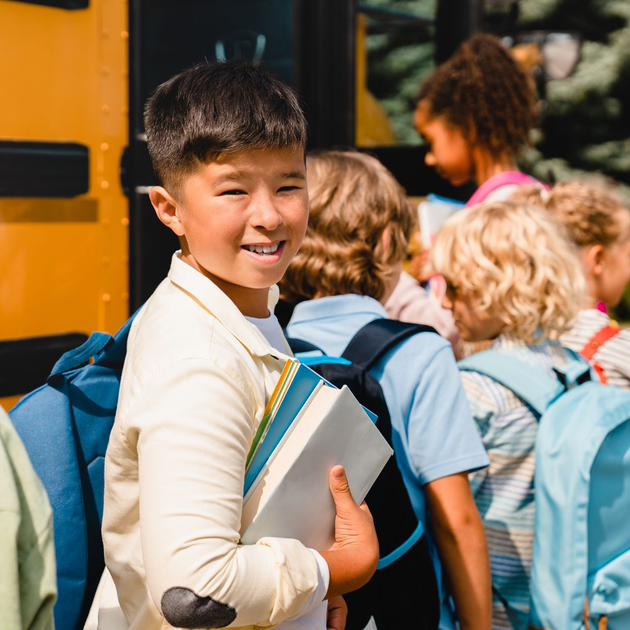 A young boy is holding a book in front of a school bus.