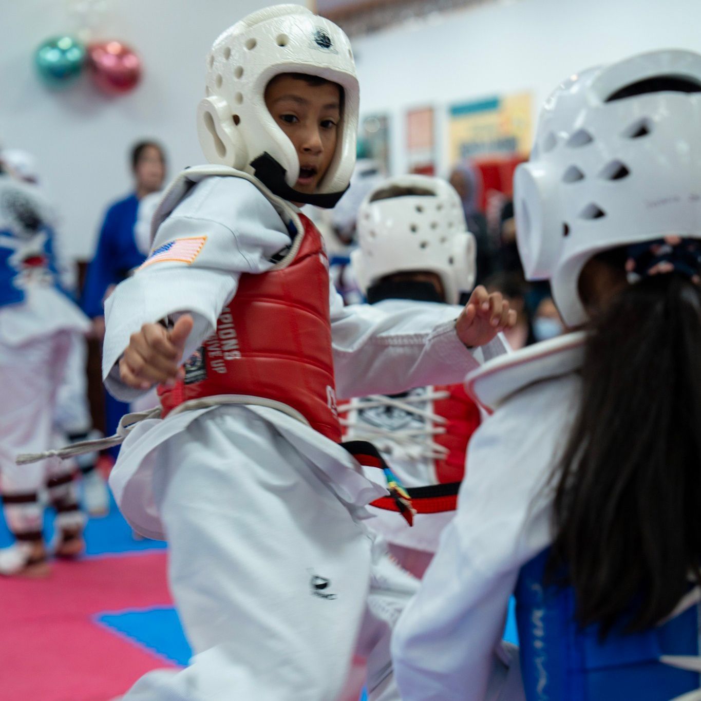 A young boy wearing a white helmet and a red vest that says taekwondo on it