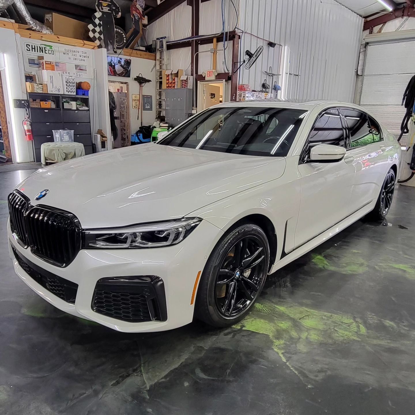 White BMW sedan in a garage, black wheels, tinted windows.