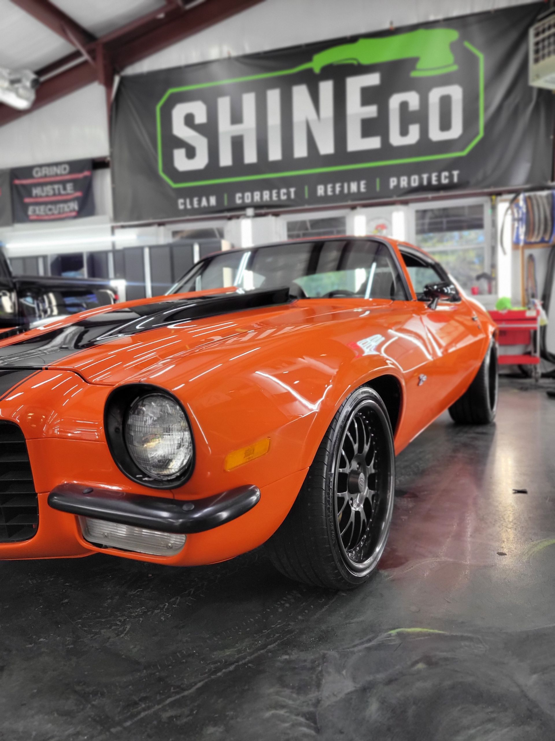 Orange classic Chevrolet Camaro in a car detailing shop.