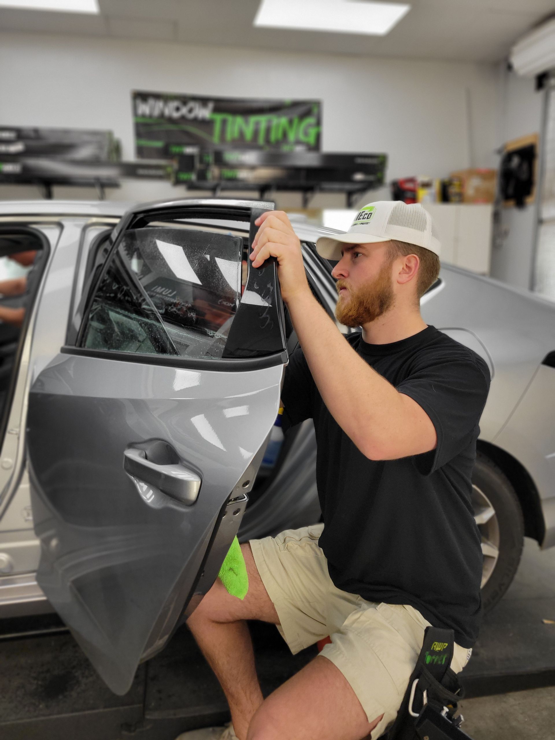 Technician installing window tint film on car door glass in auto tinting shop