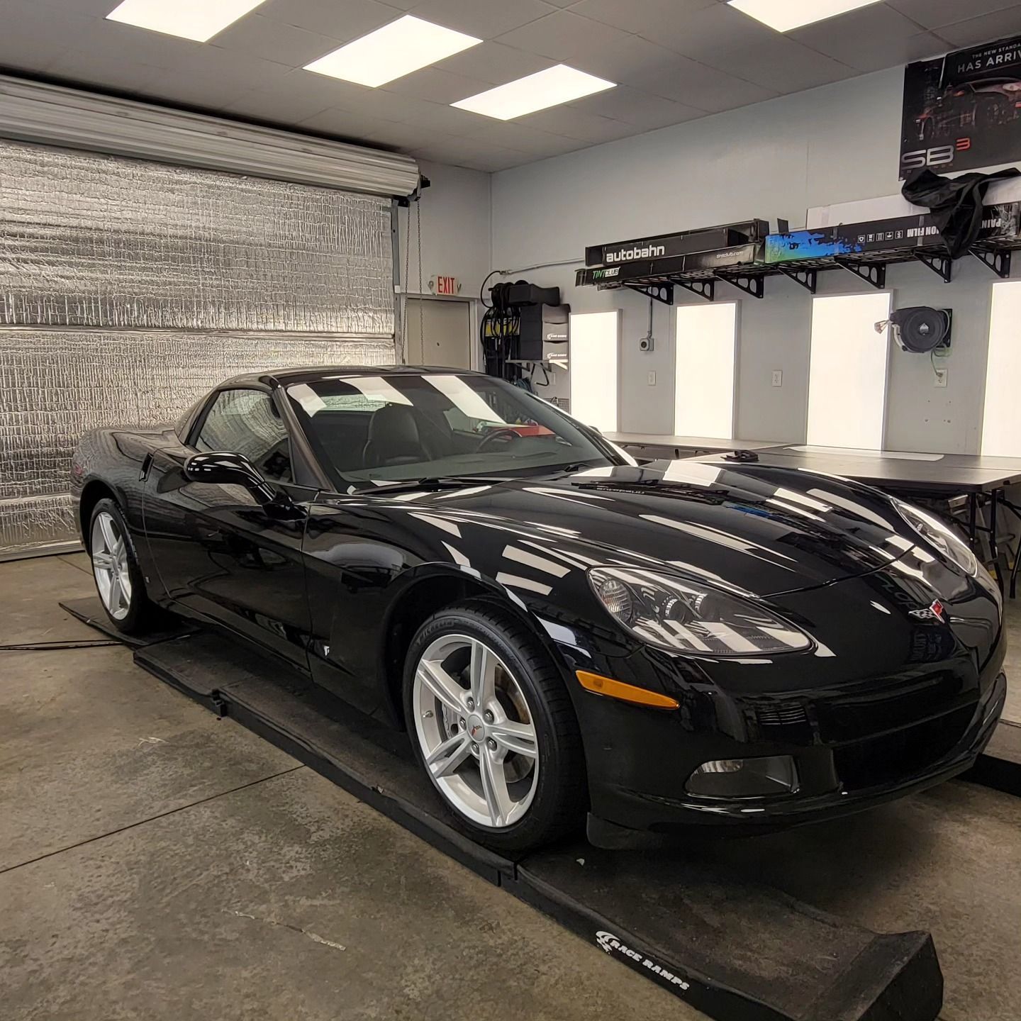 Black Corvette convertible inside a shop, parked on a lift.
