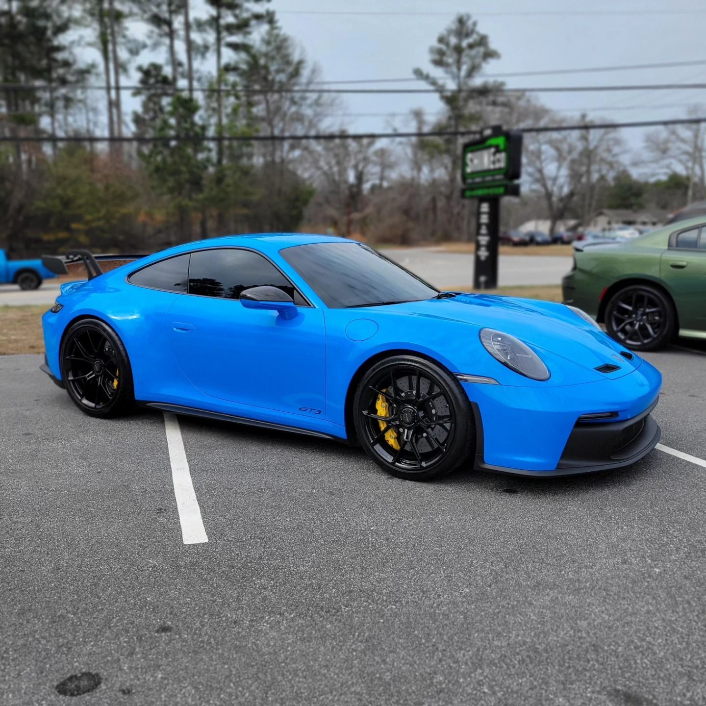 A bright blue Porsche 911 GT3 parked in an asphalt lot with black wheels and yellow brake calipers.