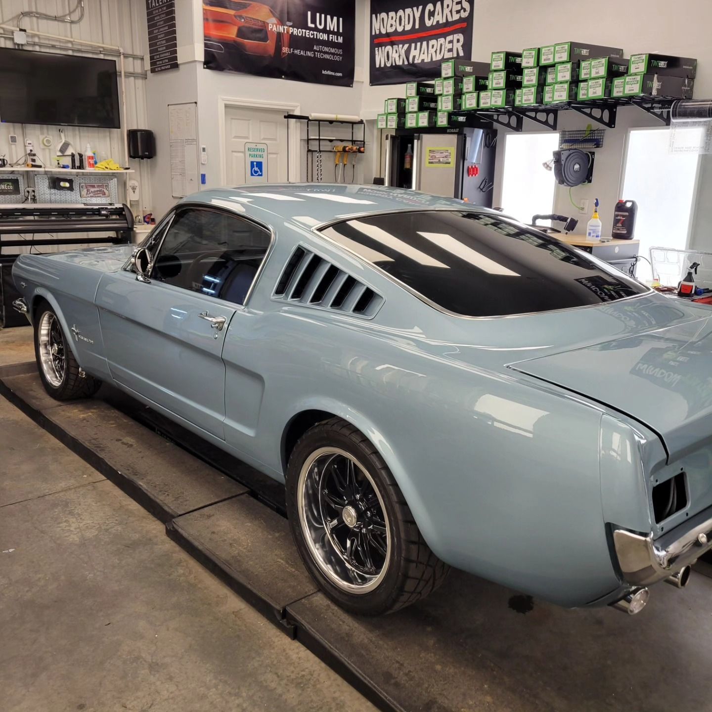 A light blue classic Ford Mustang fastback parked inside a professional automotive garage.