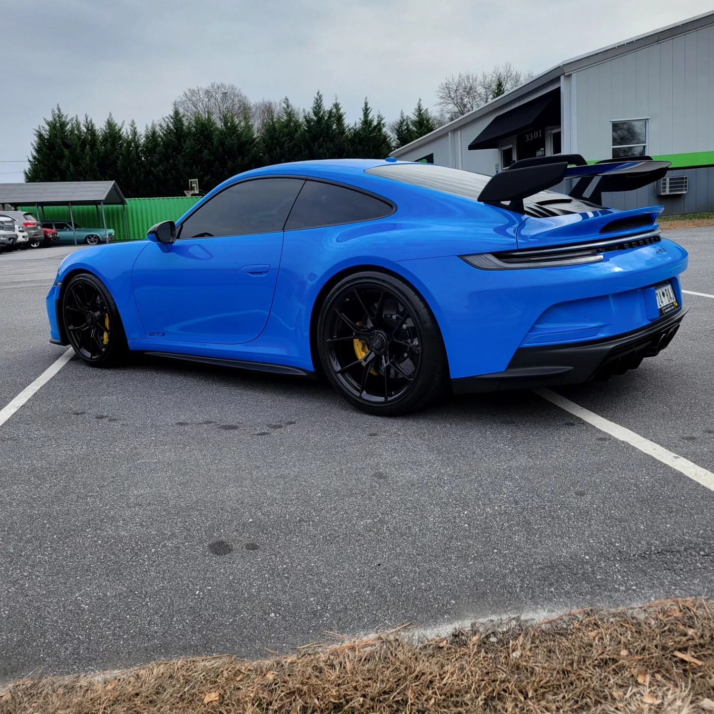 A bright blue Porsche 911 GT3 with a large rear wing parked in an asphalt lot.