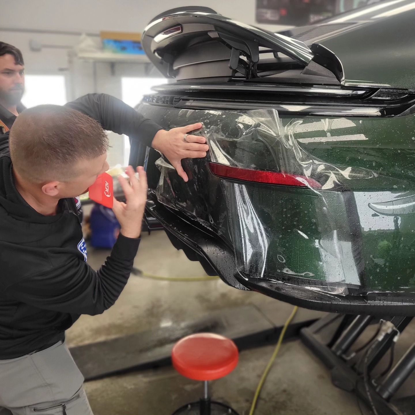 Person applying tinted film to a car window. Using tools, in a garage.