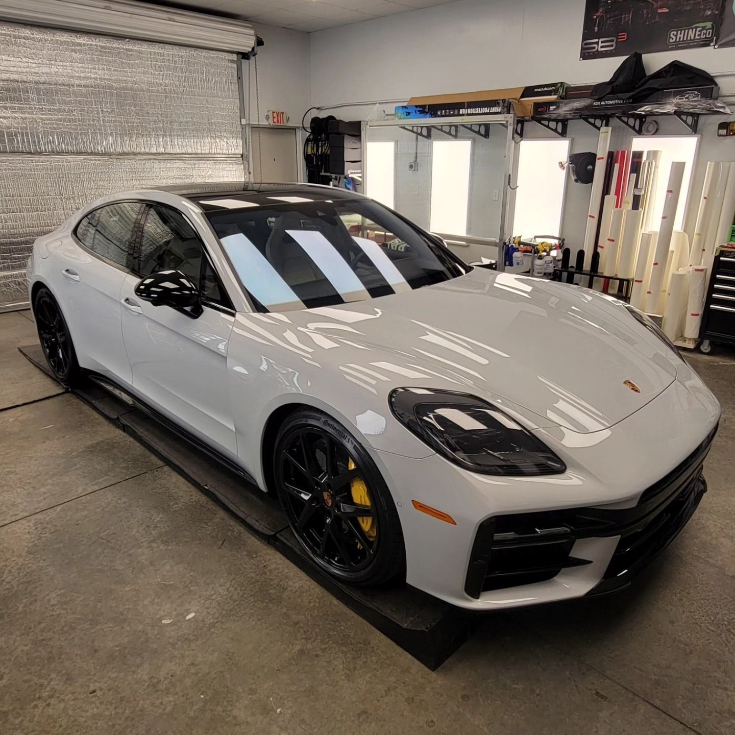 A light grey Porsche Panamera with black rims and yellow brake calipers parked inside a professional automotive shop.