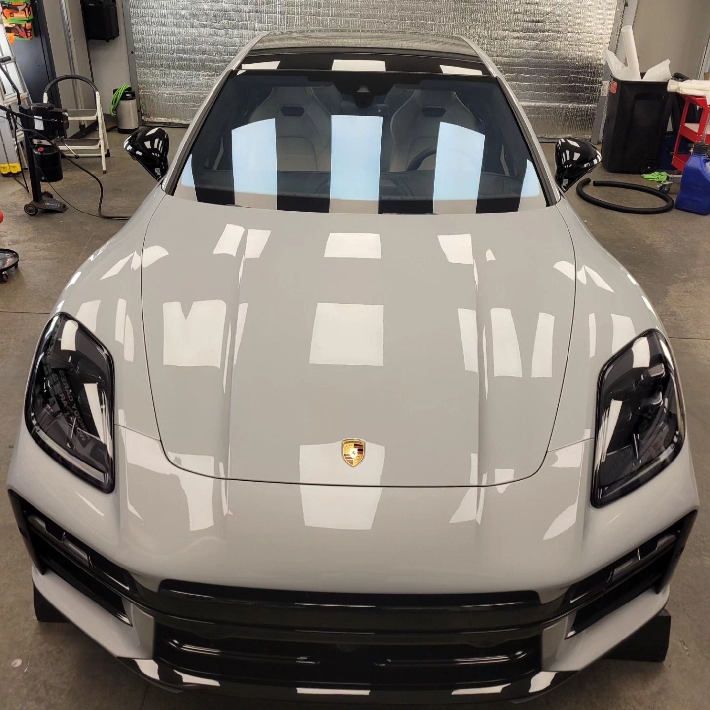 A light grey Porsche with a black roof and black trim parked inside a garage.