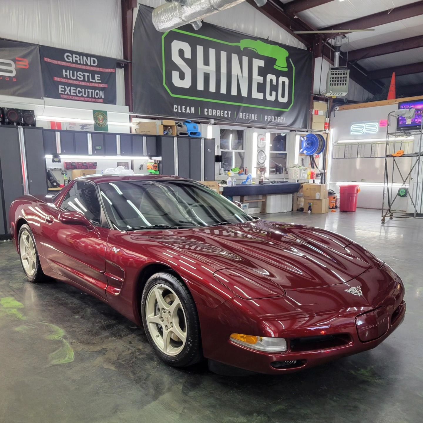 A maroon Chevrolet Corvette parked inside an auto shop with a 