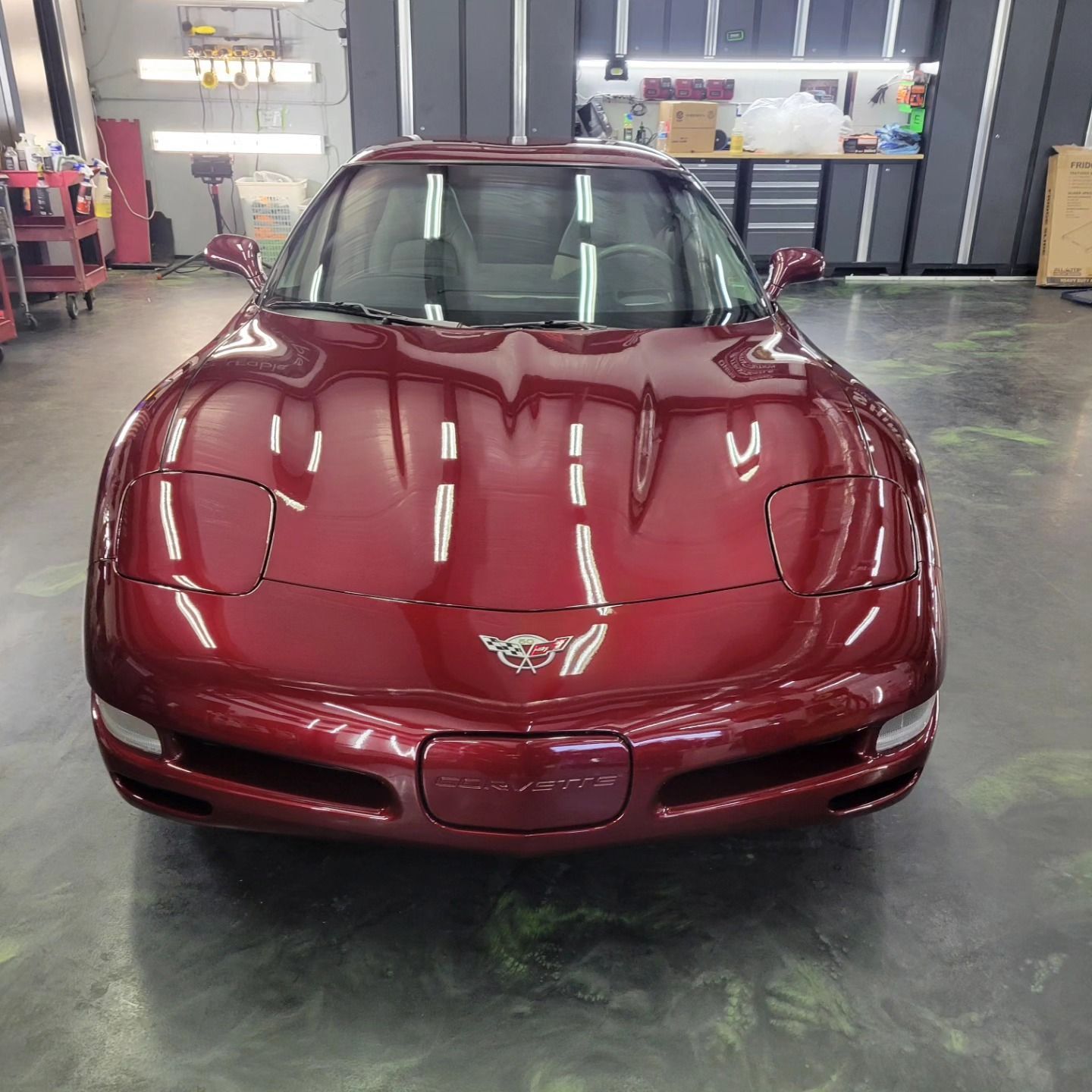 A shiny, deep red Chevrolet Corvette parked in a clean, well-lit garage with concrete floors.