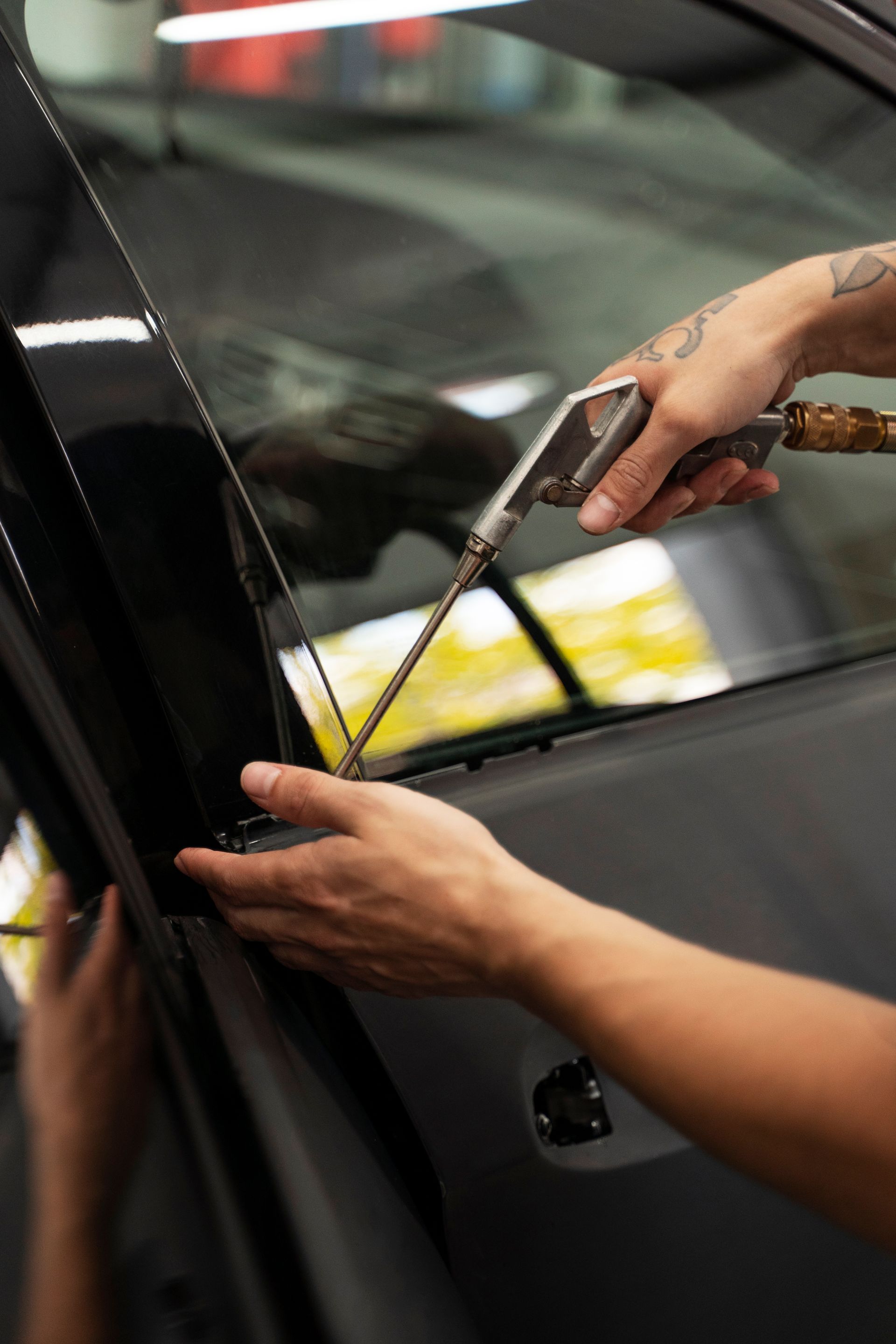 Person using a spray gun to apply tint to a car window in a garage.
