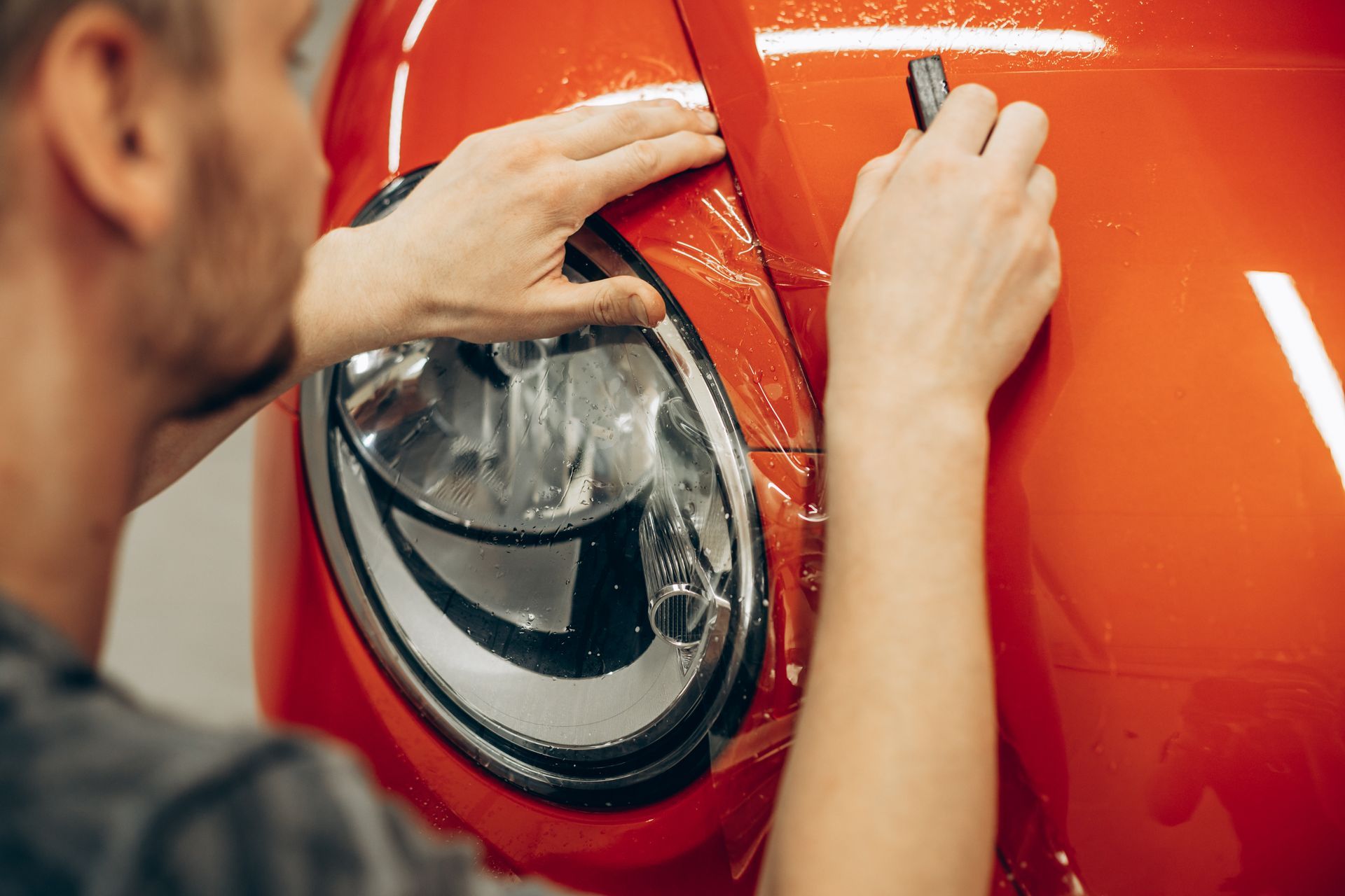 Person applying film to a red car's headlight.