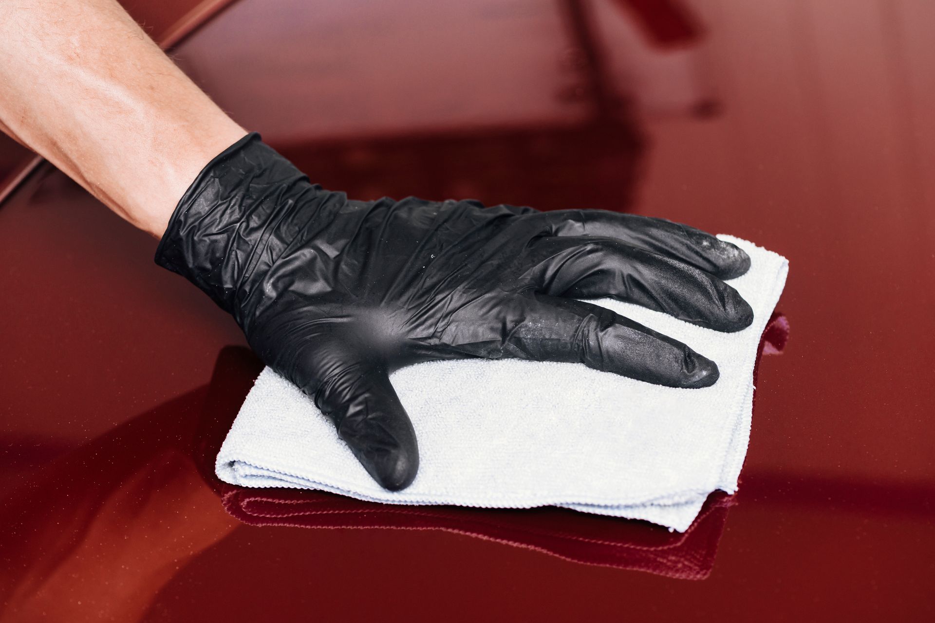 Gloved hand wiping a maroon car surface with a white cloth.
