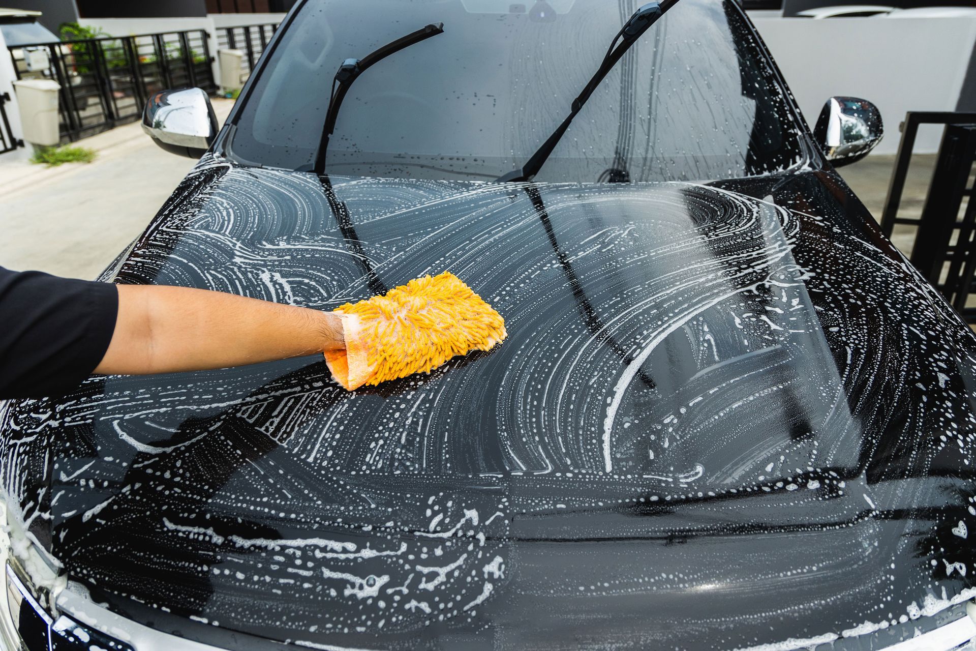 Hand washing a black car with a yellow sponge covered in soapy water.