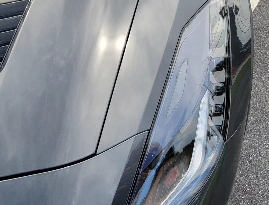 Close-up of a gray sports car's hood and headlight, reflecting the sky.