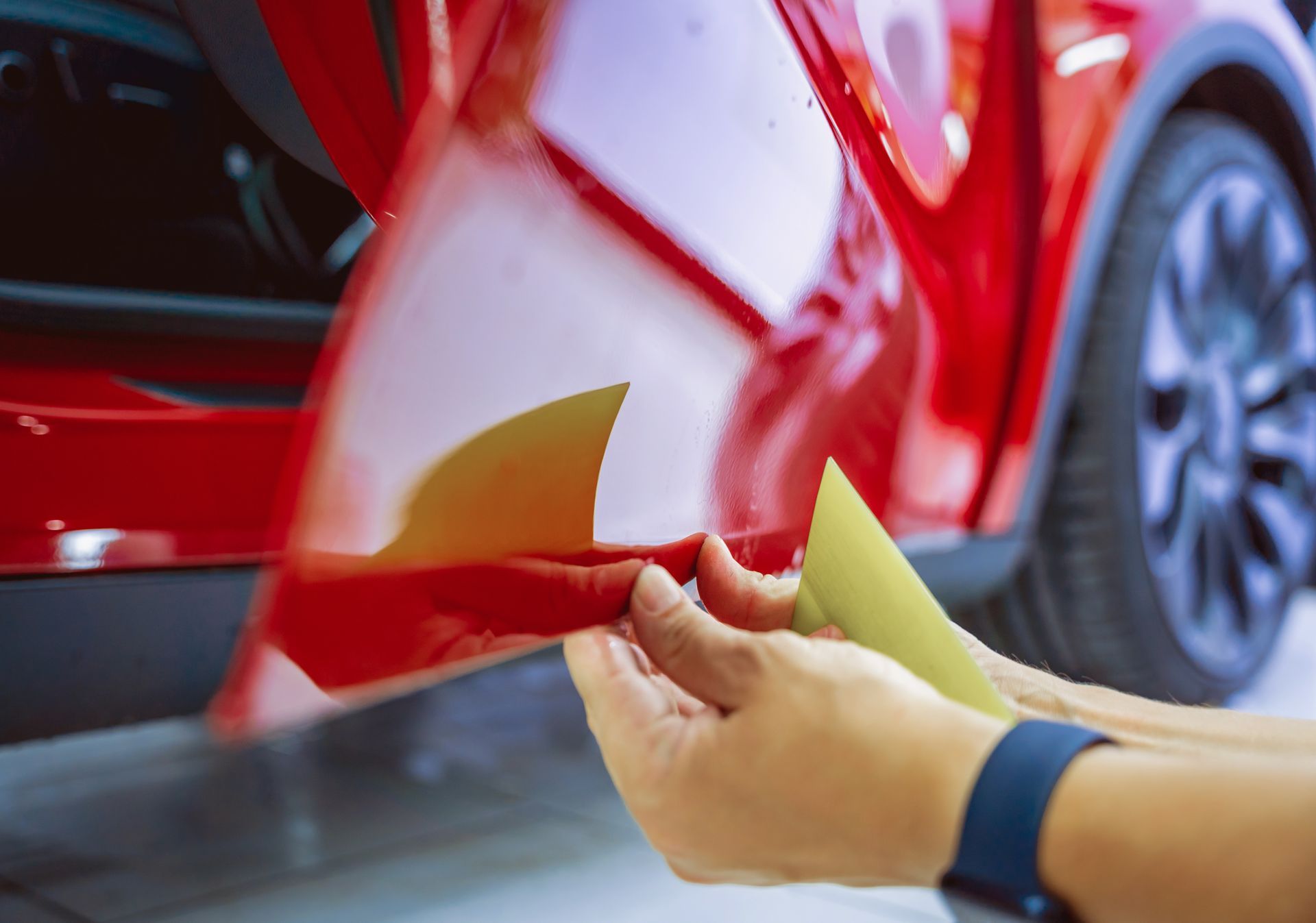 Technician removing color change PPF from a red vehicle to protect factory paint.