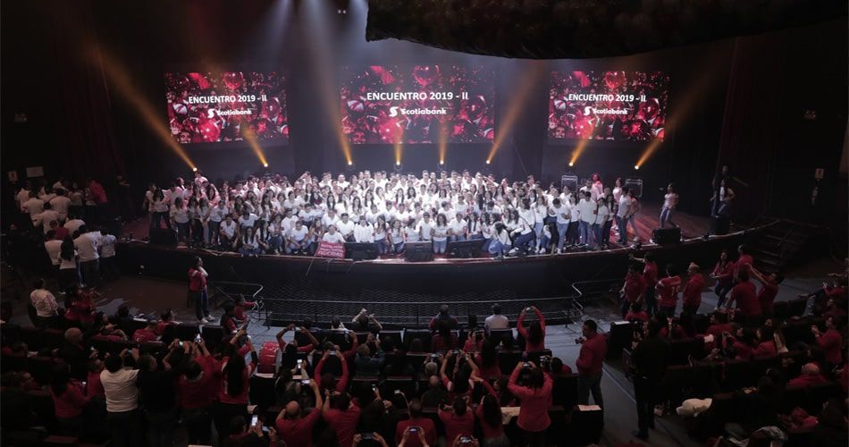 Un gran grupo de personas se encuentra frente a un escenario.