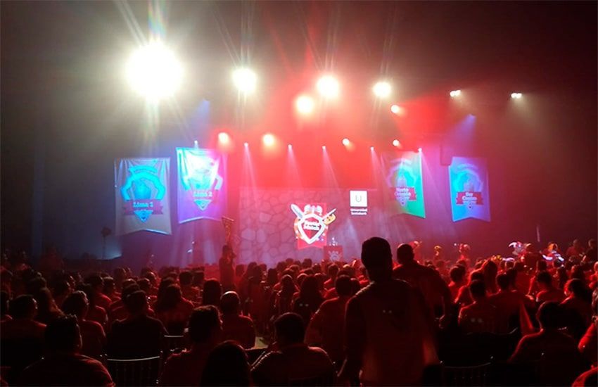 Una multitud de personas sentadas frente a un escenario con una abeja encima.