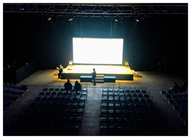 La gente está parada en un escenario en un auditorio oscuro