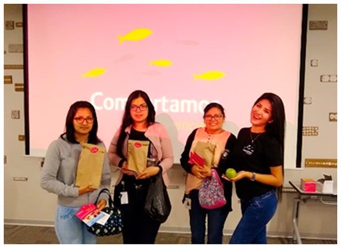 Un grupo de mujeres paradas frente a una pantalla que dice "compartimos"