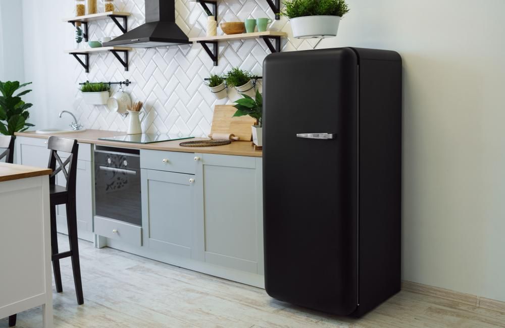 A Black Refrigerator Is Sitting in The Middle of A Kitchen — JDG Refrigeration & Air in Goonellabah, NSW