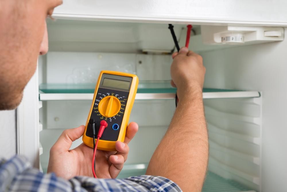 A Man Is Using a Multimeter to Fix a Refrigerator — JDG Refrigeration & Air in Bangalow, NSW