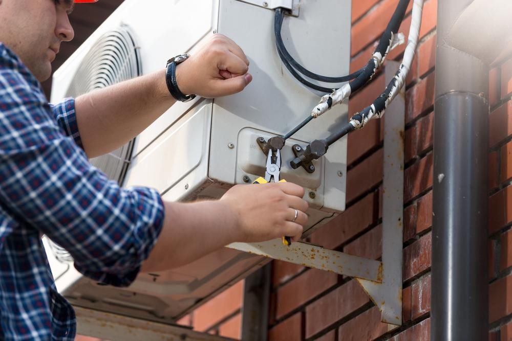 A Man Is Fixing an Air Conditioner on A Brick Wall — JDG Refrigeration & Air in Casino, NSW