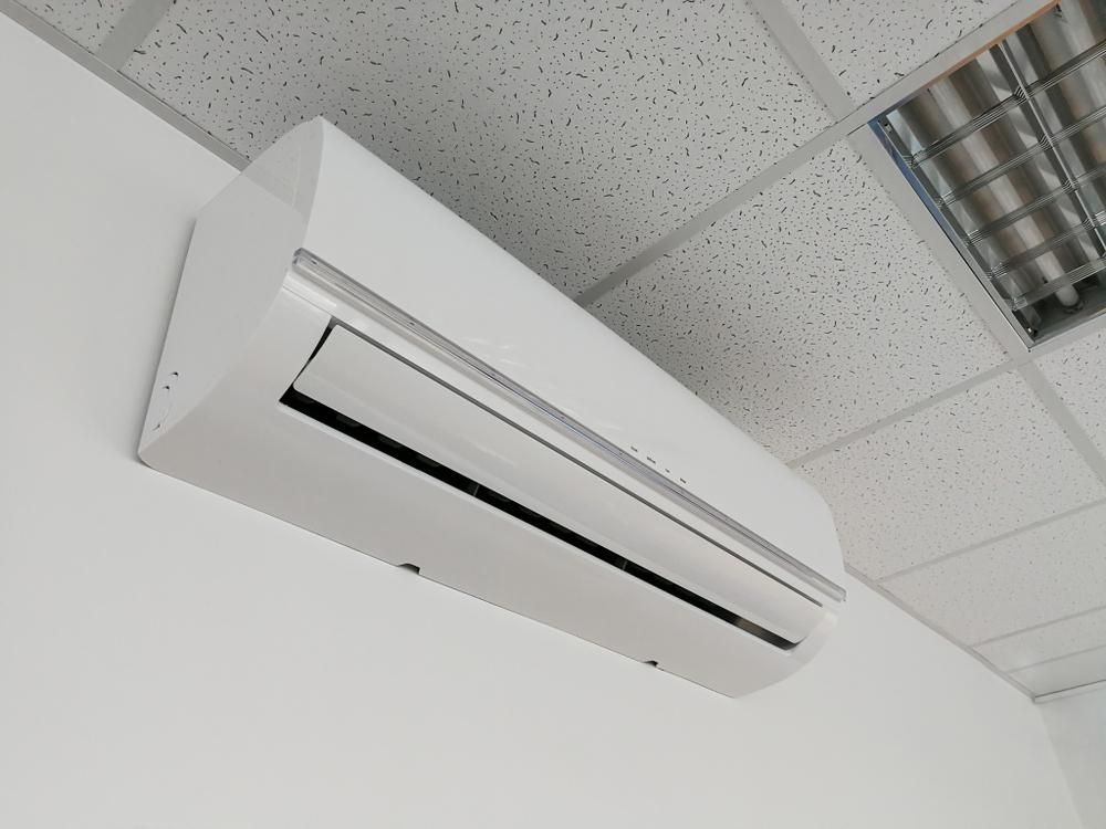 A White Air Conditioner Is Mounted on A White Wall — JDG Refrigeration & Air in Goonellabah, NSW