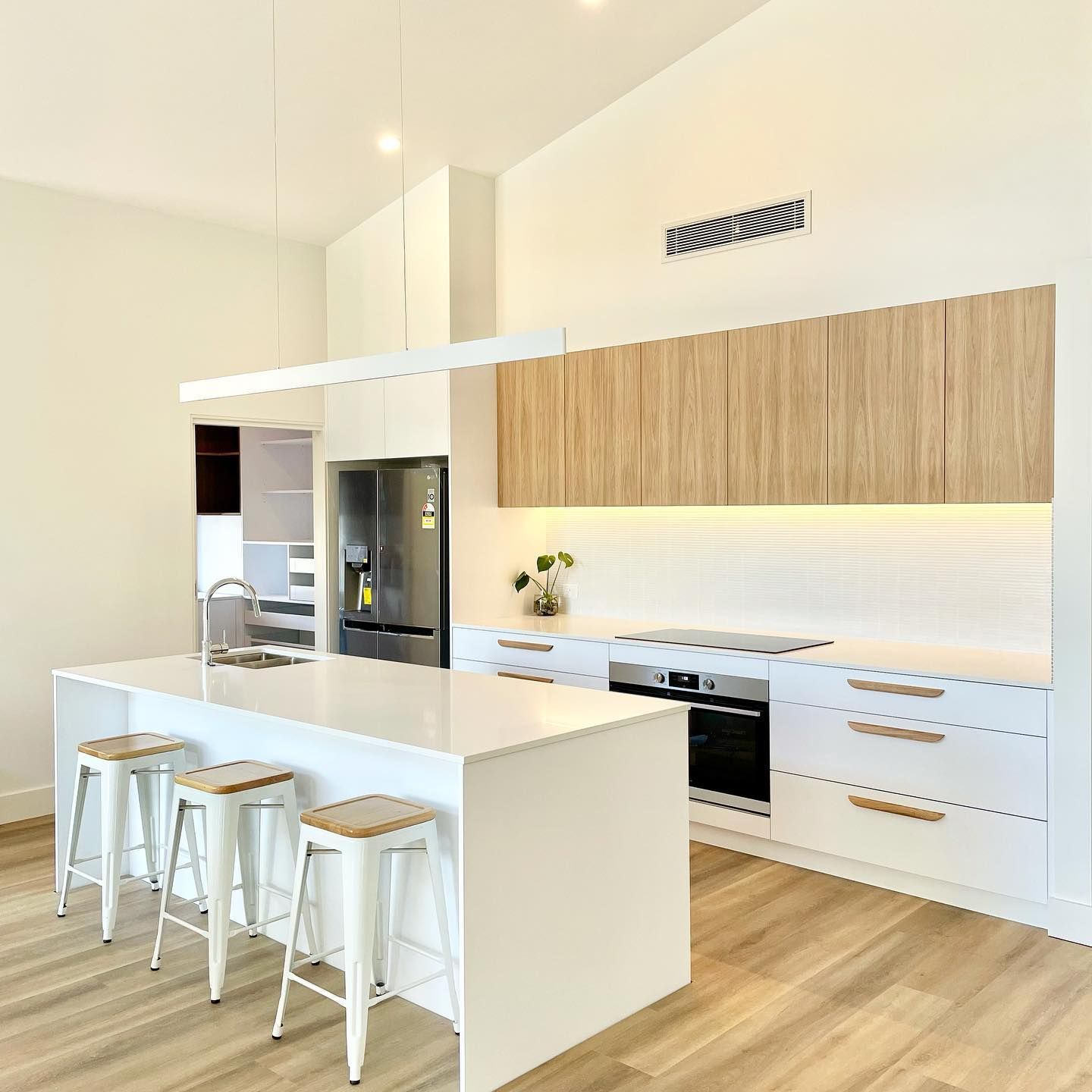 Modern white kitchen with island seating, light wood cabinets, stainless steel refrigerator — BSpoke Cabinet Making & Joinery in Unanderra, NSW