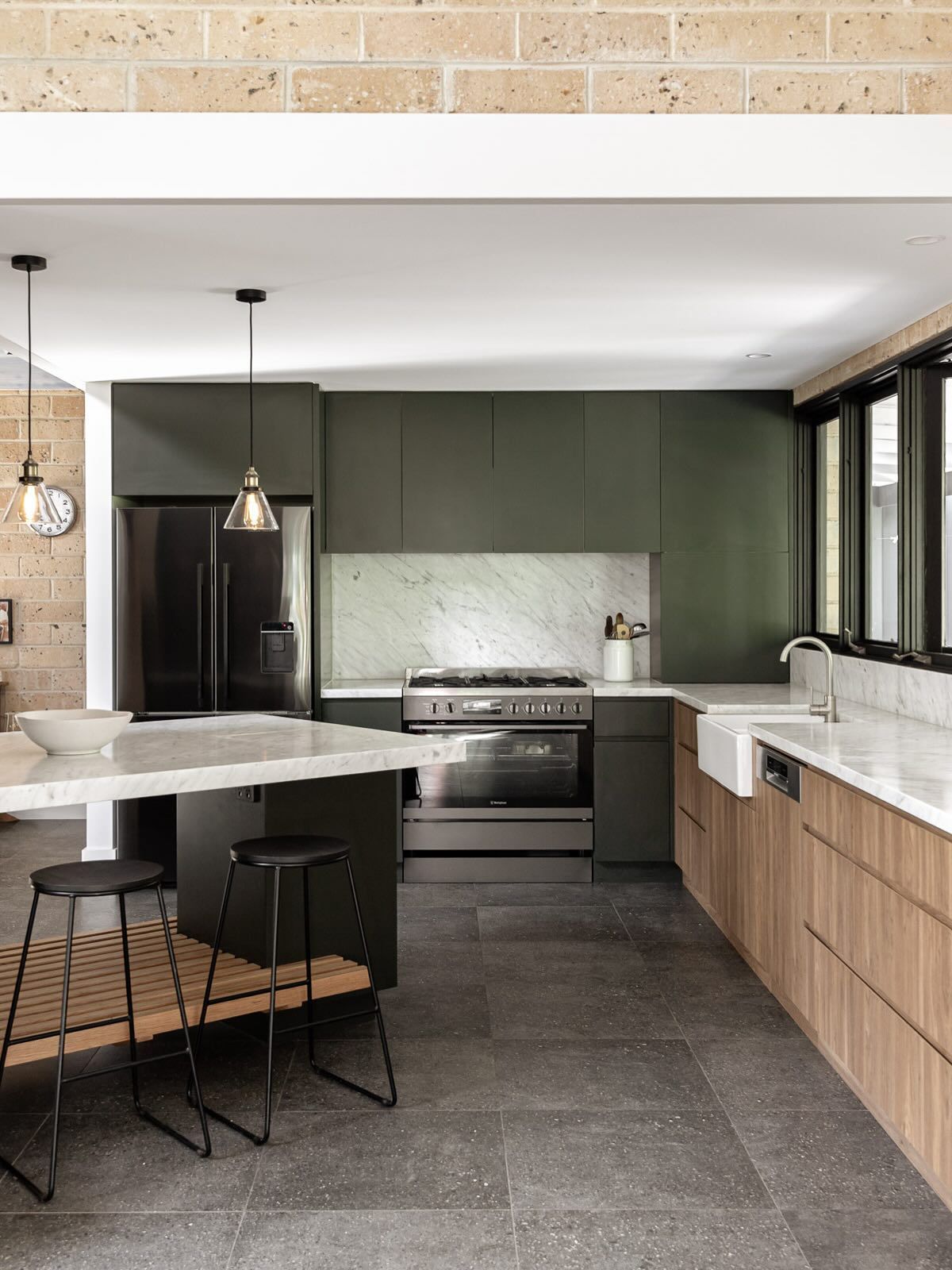 Modern kitchen with dark green cabinets, marble backsplash, island with stools, and stone flooring — BSpoke Cabinet Making & Joinery in Shellharbour, NSW