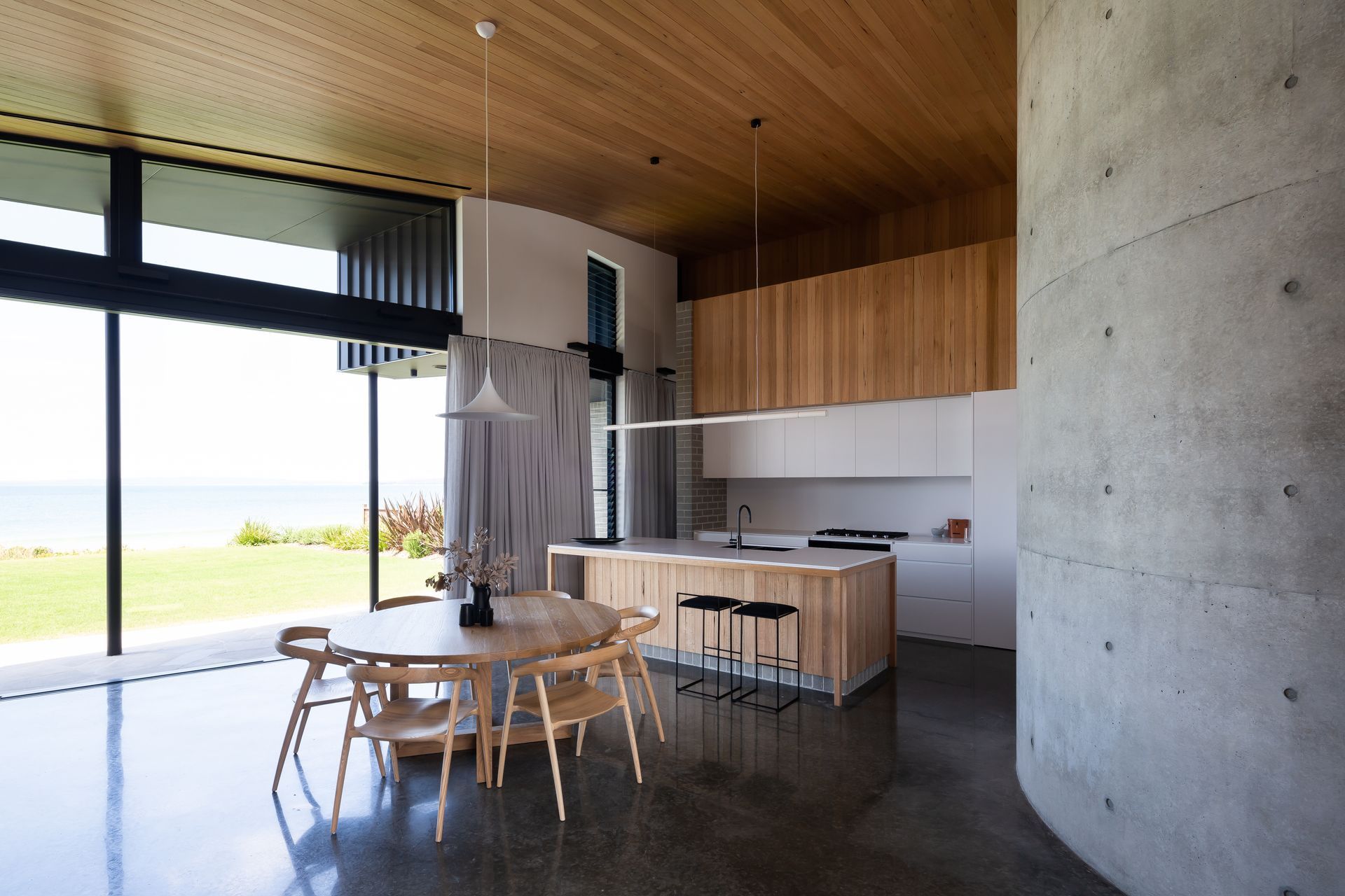 Modern kitchen and dining area with ocean view, wooden accents, and concrete wall — BSpoke Cabinet Making & Joinery in Unanderra, NSW
