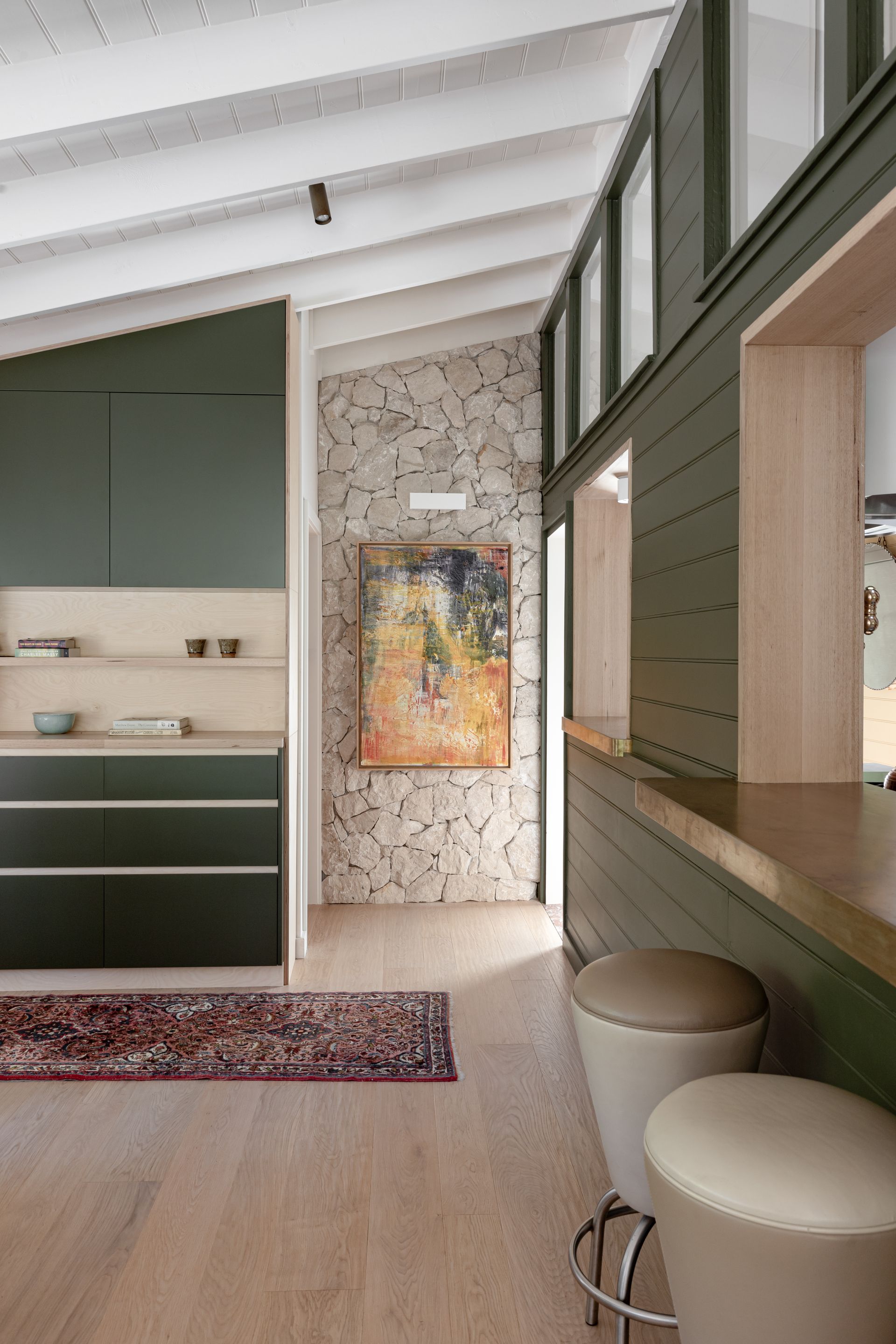Interior kitchen view with green cabinets, stone wall, and bar with stools — BSpoke Cabinet Making & Joinery in Southerland Shire, NSW
