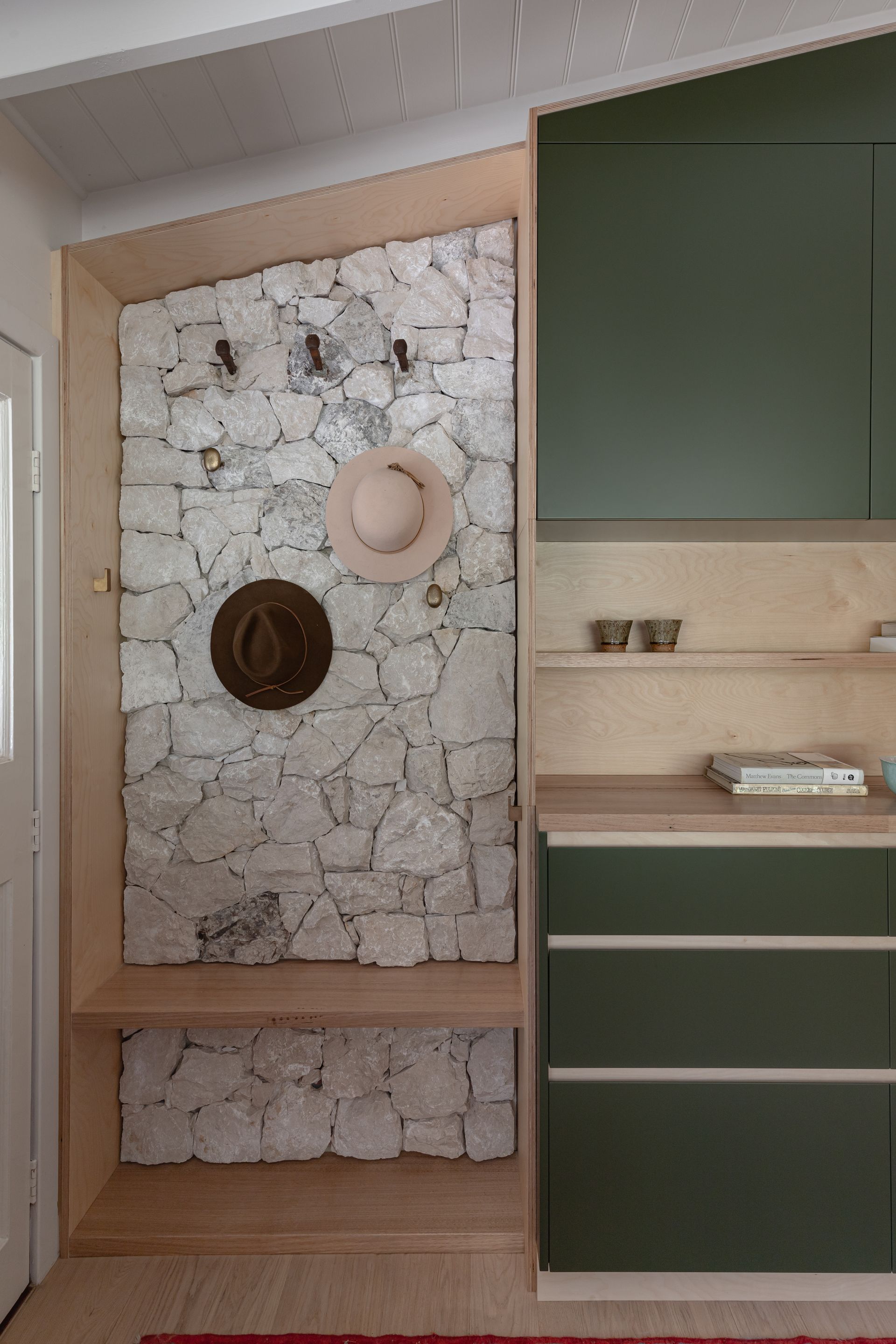 Entryway with stone wall, wooden shelf and trim. Green cabinets to the right. Hats hanging on wall — BSpoke Cabinet Making & Joinery in Unanderra, NSW