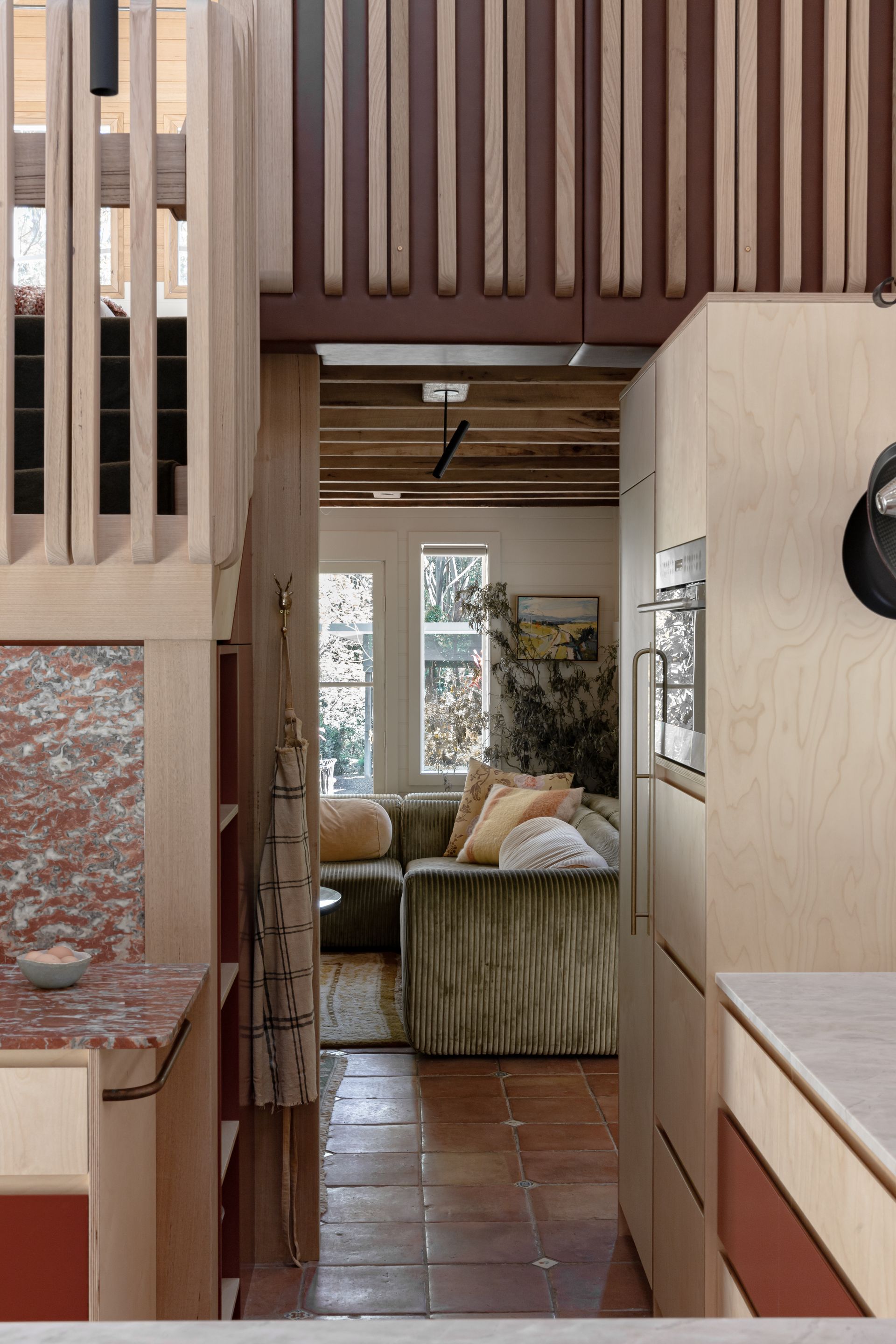 Interior with warm tones. A small kitchen leads to a living area with a green sofa — BSpoke Cabinet Making & Joinery in Unanderra, NSW