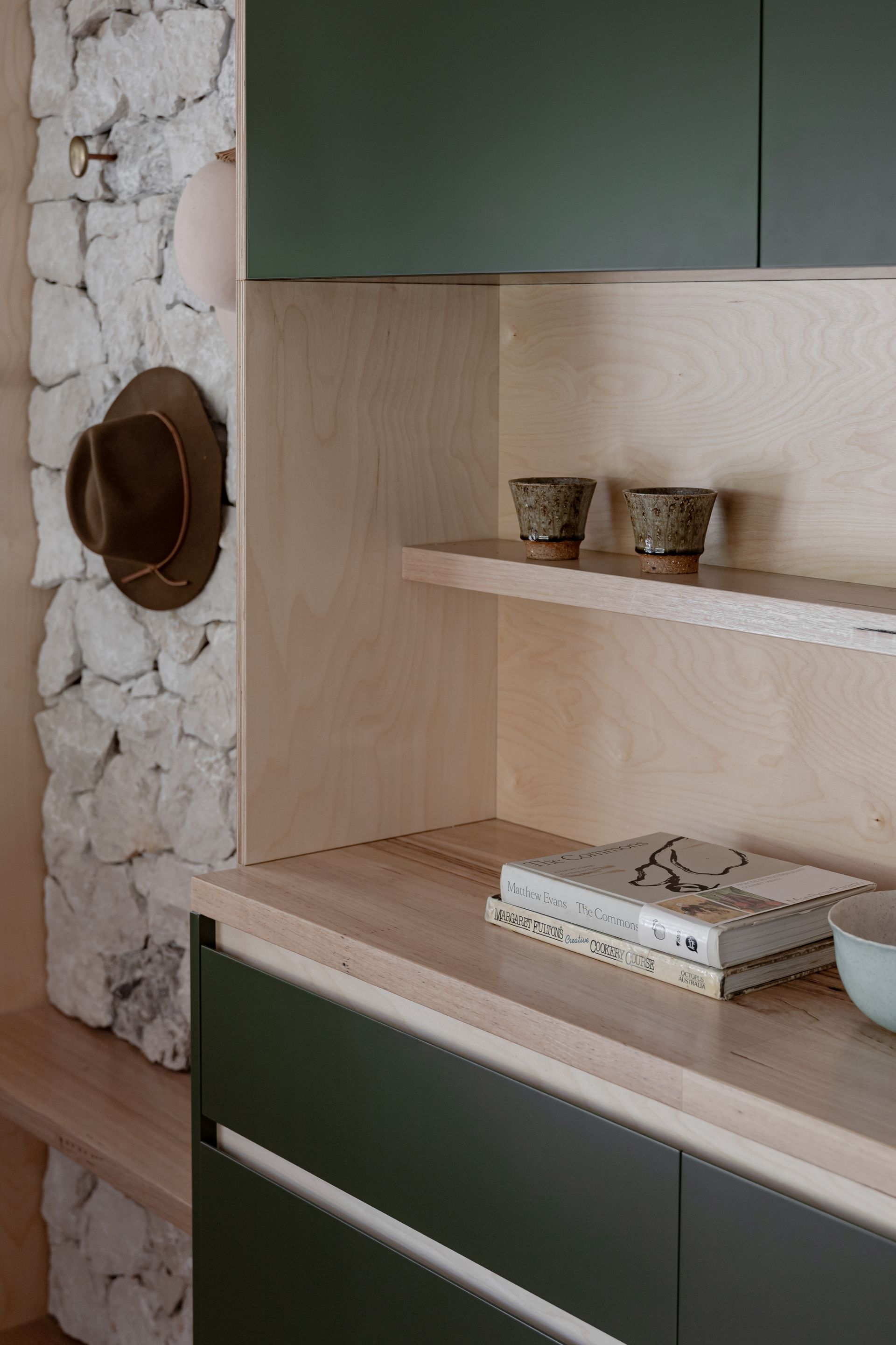 Built-in shelving and cabinets with light wood accents and dark green doors. Stone wall and hat to the left — BSpoke Cabinet Making & Joinery in Southerland Shire, NSW