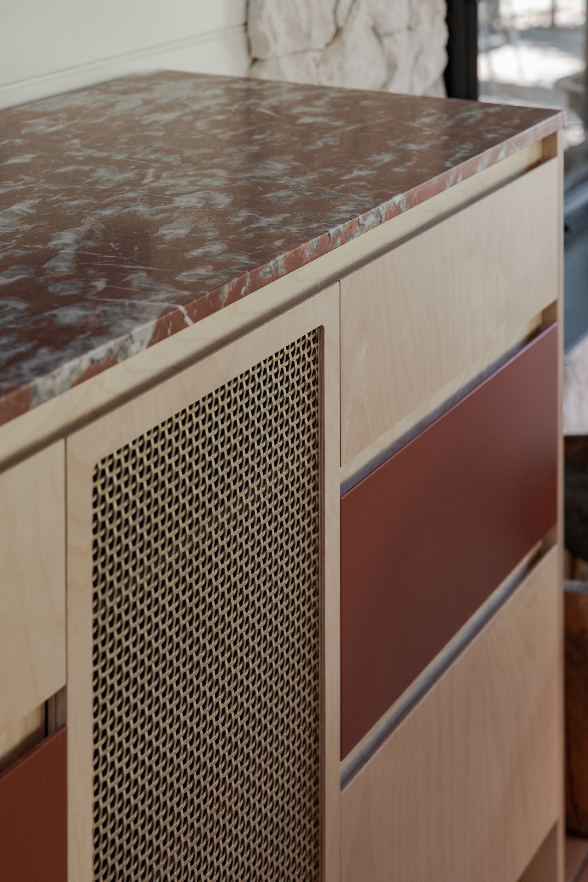 Close-up of a wooden cabinet with a reddish-brown marble top, a perforated panel, and a red drawer — BSpoke Cabinet Making & Joinery in Unanderra, NSW