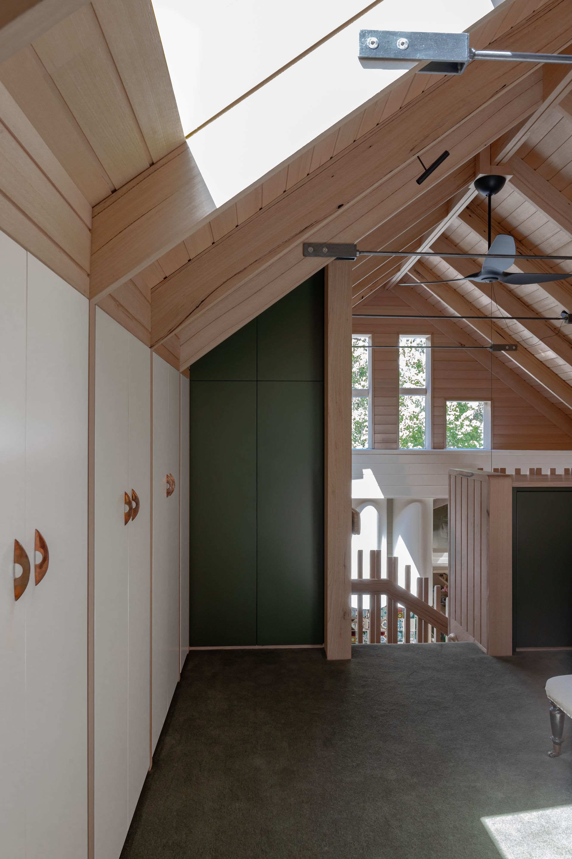 Interior of a room with slanted wooden ceiling, skylight, white closet doors with copper handles, and dark green door — BSpoke Cabinet Making & Joinery in Southerland Shire, NSW