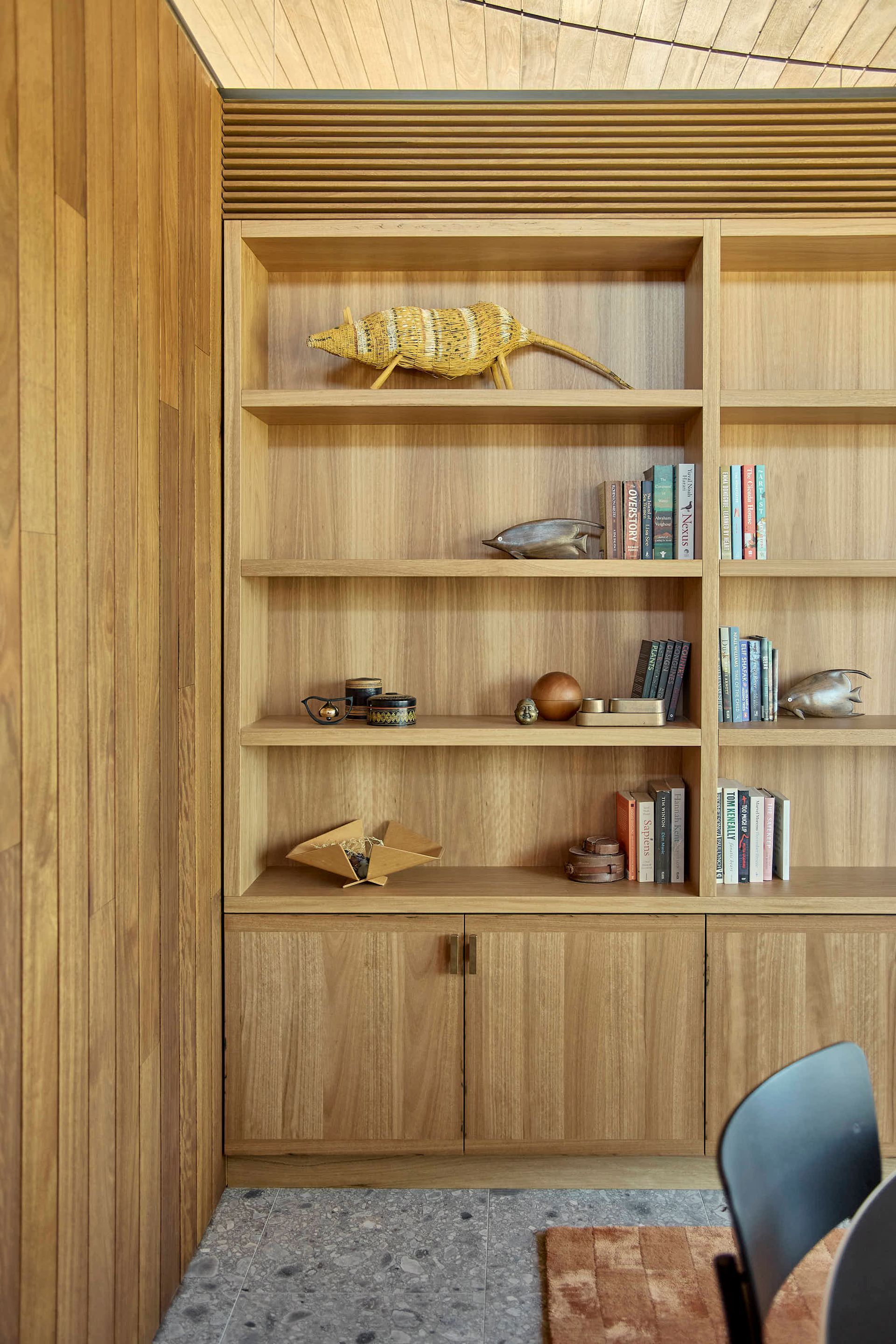 Wooden built-in shelving unit with books and decor items. Located in a room with wood paneling and a patterned floor — BSpoke Cabinet Making & Joinery in Southerland Shire, NSW