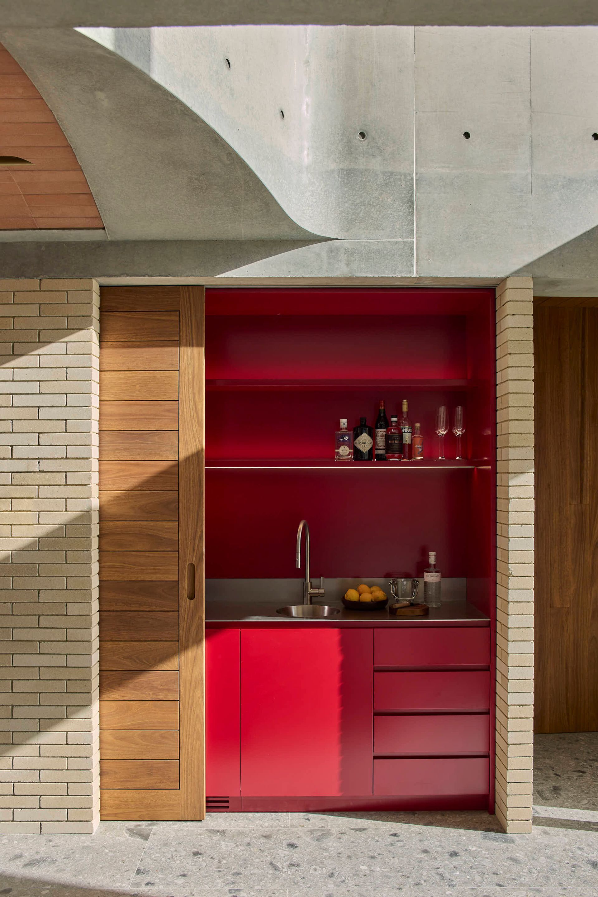A red-painted bar area built into brick wall with wooden sliding door and concrete ceiling — BSpoke Cabinet Making & Joinery in Unanderra, NSW