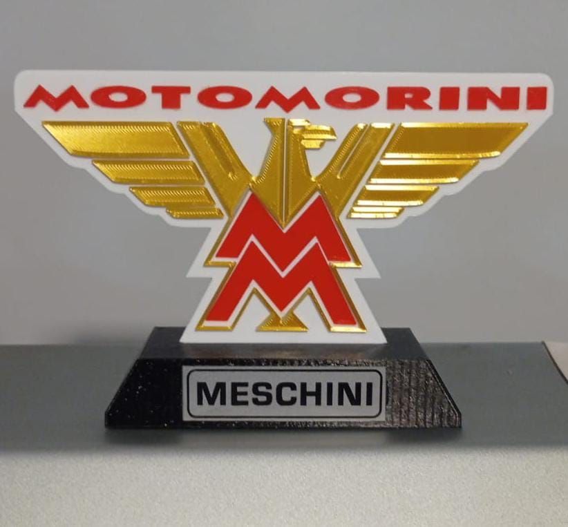 Un logotipo de Motomorini rojo y dorado se encuentra sobre una base negra.