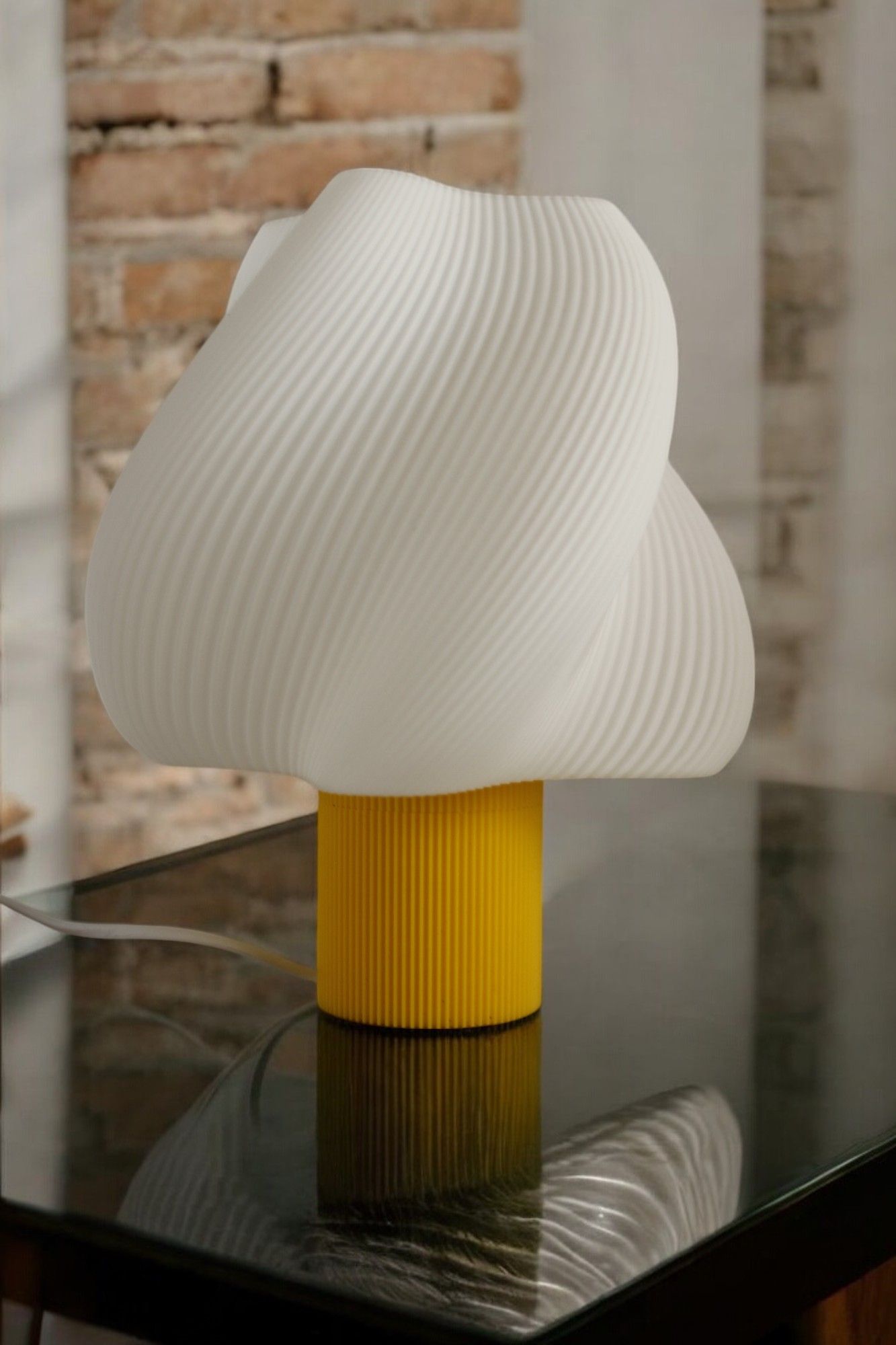 Una lámpara blanca con una base amarilla está sobre una mesa de cristal.