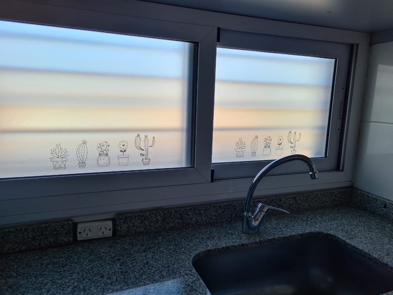 Ventana de cocina con película esmerilada, siluetas de cactus, fregadero y grifo. Encimera de granito.
