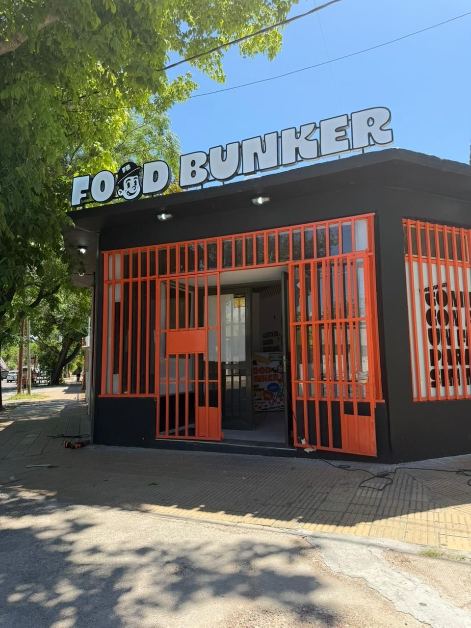 Fachada del restaurante Food Bunker, con detalles en negro y naranja, sobre una acera, bajo un cielo azul.