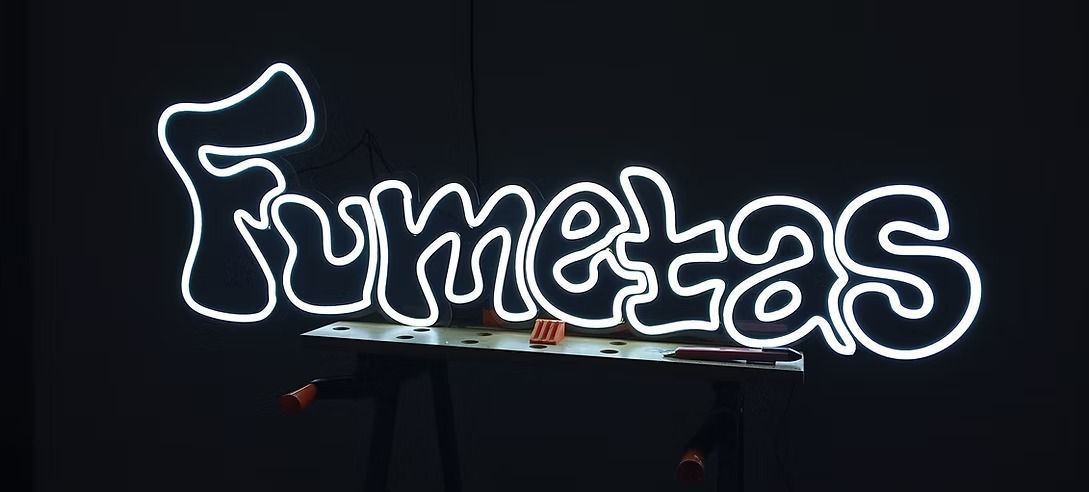 Un letrero de neón que dice fumelas sobre un fondo negro.