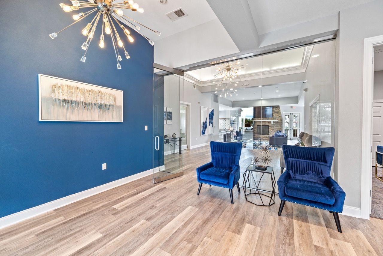 Modern apartment community lobby with blue accent wall, glass doors, and blue velvet chairs.